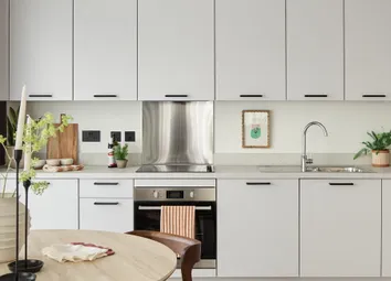 Wooden Dining Table In Foreground, Kitchen Behind With White Cupboard Panels And White Counters.