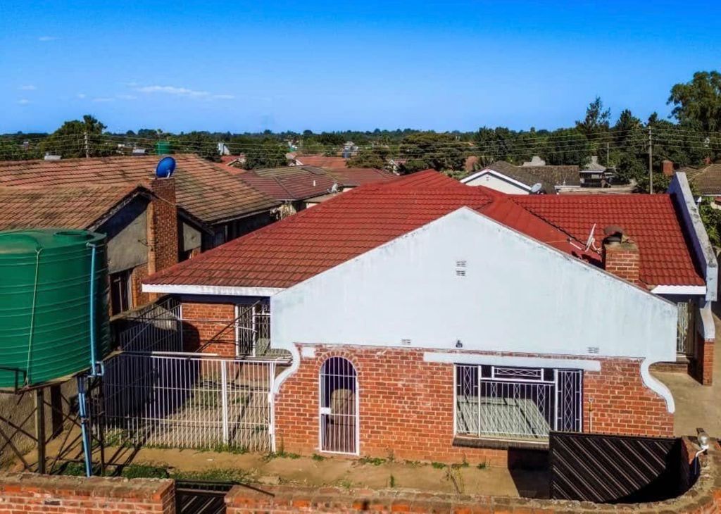 Property photo 1 of 6 Front View Of A Brick House With A Red-Tiled Roof, White Upper Wall, And A Metal Gate In A Residential Neighborhood.