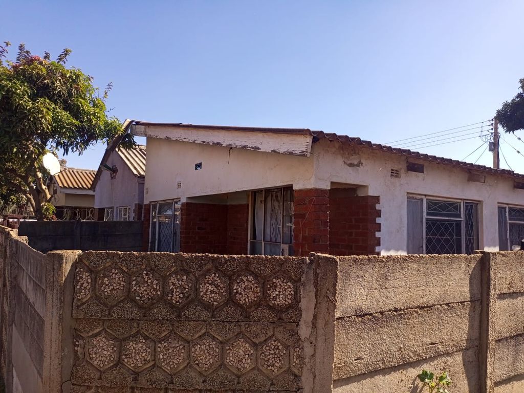Property photo 1 of 12 A Single-Story House With White Walls And Red Brick Accents Behind A Textured Concrete Wall On A Sunny Day, With A Clear Blue Sky And A Tree On The Left.