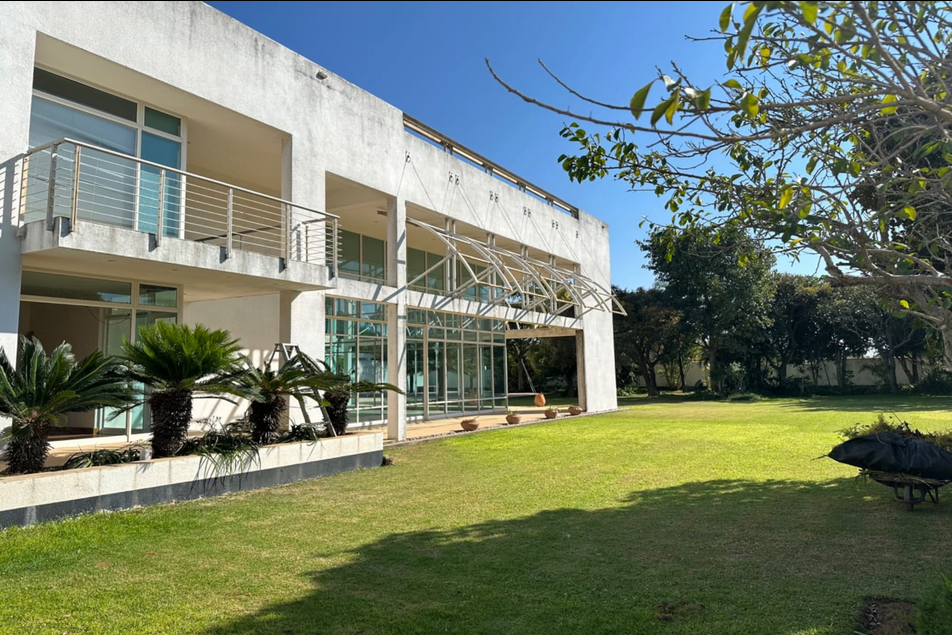 Property photo 3 of 24 Modern White Two-Story Building With Glass Doors, Balcony, And A Manicured Lawn Under A Blue Sky, Trees In The Background.