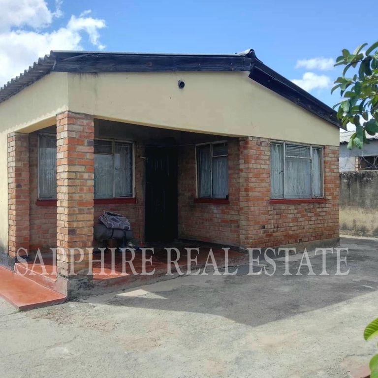 Property photo 1 of 18 Single-Story Brick House With A Small Front Porch, Black Door, And Two Windows With Metal Bars Under A Blue Sky