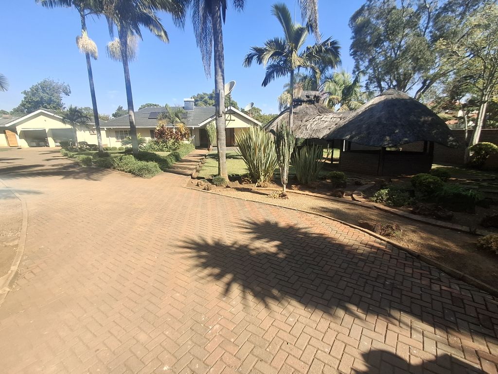 Property photo 1 of 14 A Sunny Residential Scene With A Curved Brick Path, Palm Trees, And A Thatched-Roof Gazebo Beside Single-Story Houses Under A Blue Sky.