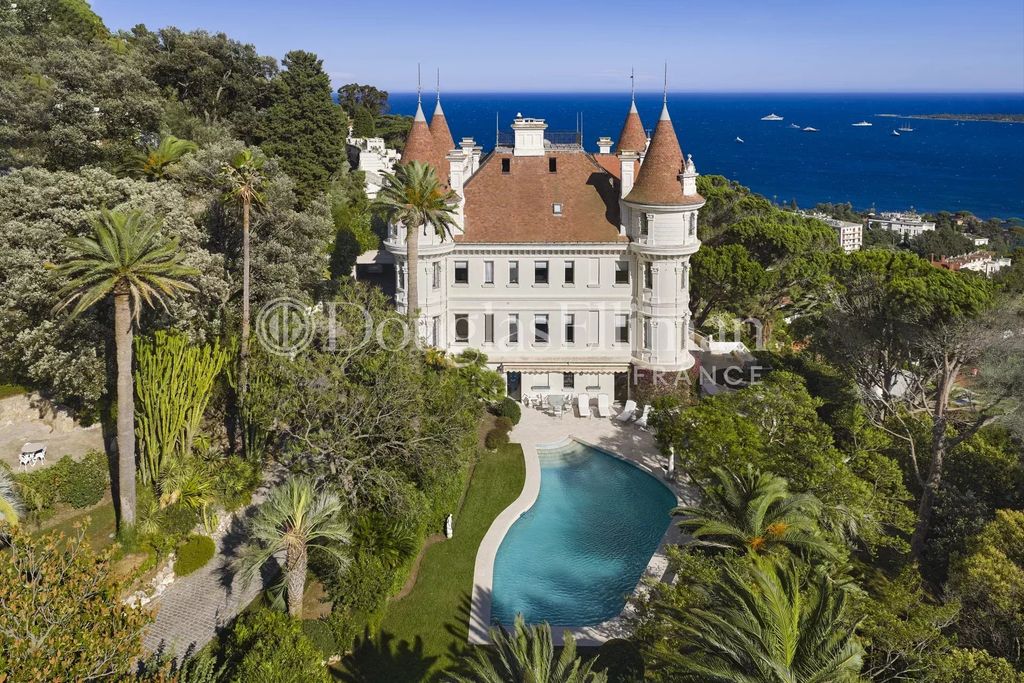 Property photo 1 of 12 A Grand, Castle-Like Mansion With Towers And A Red Roof Overlooks A Lush Garden With A Winding Pool, Set Against A Backdrop Of The Sea And Distant Boats.