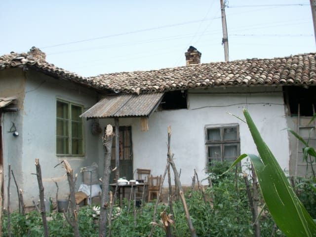 Property photo 1 of 34 Exterior View Of A Traditional Bulgarian Village House With A Tiled Roof And Garden Plants Enclosed By A Rustic Wooden Stick Fence.