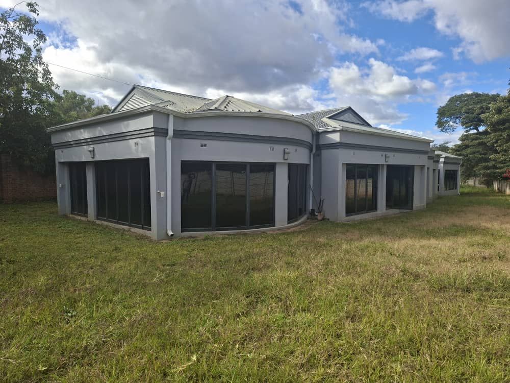 Property photo 1 of 19 Modern Gray Building With Curved Glass Walls And A Grassy Field In The Foreground Under A Cloudy Sky And Blue Patches.