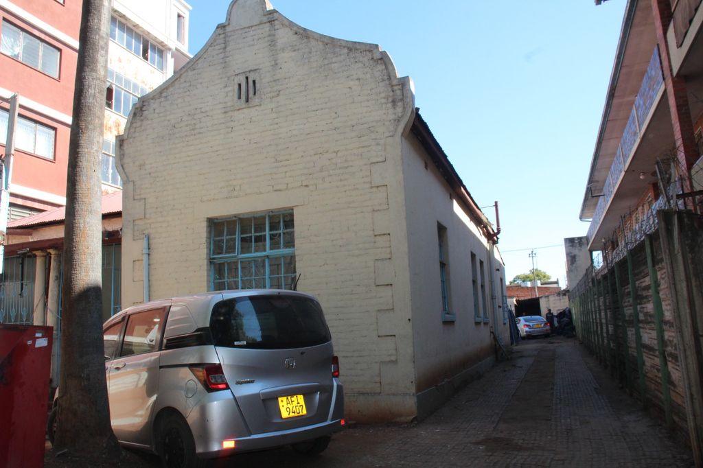 Property photo 3 of 15 Narrow Alley With Light Brick Building Featuring Arched Top, Parked Silver Car, And Palm Tree On Left Under A Clear Blue Sky