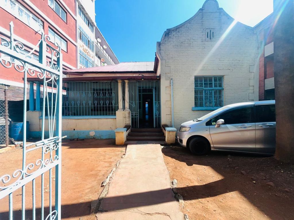 Property photo 1 of 15 Front View Of A Small White Brick Building With A Blue Decorative Gate, Blue Window Bars, And A Silver Van Parked On The Dirt Driveway To The Right.