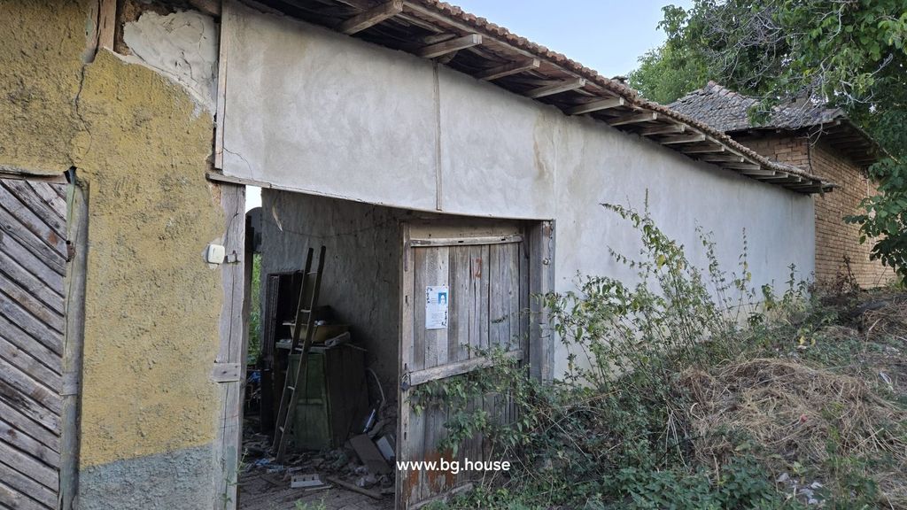 Property photo 2 of 29 Side View Of The House Showing An Open Wooden Door, Plastered Walls, And Surrounding Overgrown Vegetation.