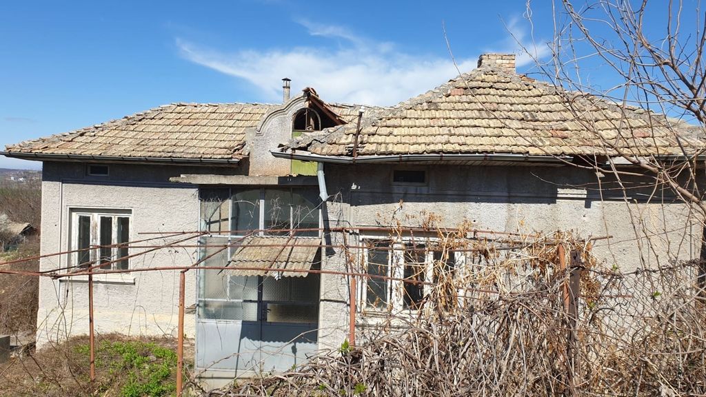 Property photo 2 of 33 Side Perspective Of A Grey Village House Featuring A Tiled Roof And An Enclosed Porch, With Dry Vegetation And Bare Branches Around The Property.