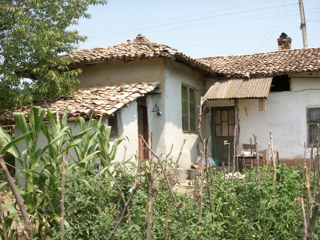 Property photo 2 of 34 Side Perspective Of The Village House Featuring A Tiled Roof, Windows, Wooden Door, And A Garden With Tall Plants And Wooden Fencing.