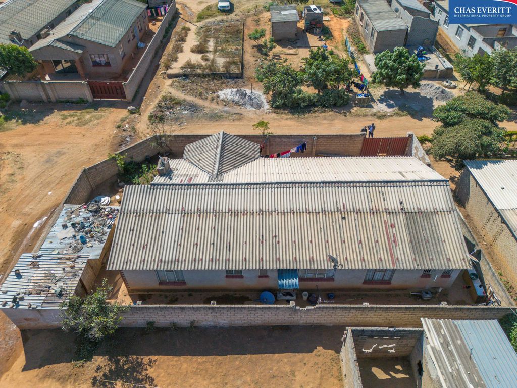 Property photo 3 of 9 Aerial View Of A Dusty Residential Area With Boxy Brick Houses, Dirt Roads, And Scattered Trees; A Large Corrugated Metal Roof Dominates The Foreground. Chas Evertt Logo Visible In The Top-Right Corner.
