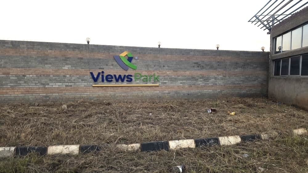 Property photo 3 of 7 Brick Wall With A 'views Park' Logo/Sign, A Bare Grassy Lot In Front, And A Glass-Walled Building To The Right.