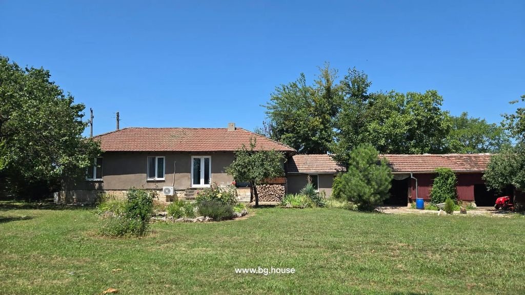 Property photo 1 of 79 A Single-Storey House With A Tiled Roof And Brown Walls, Surrounded By A Green Lawn, Trees, And Garden Beds Under A Clear Blue Sky.