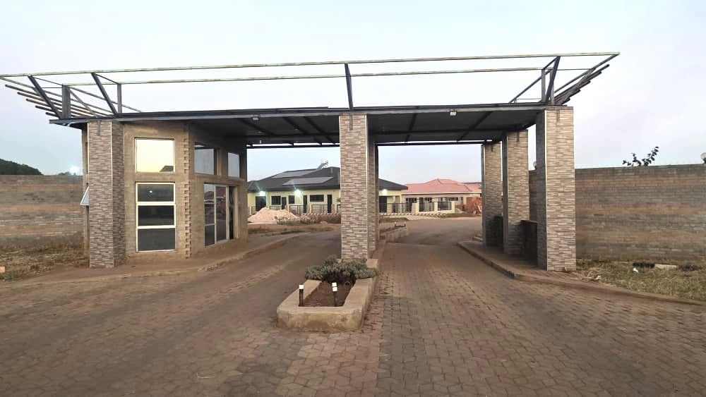 Property photo 2 of 7 Brick-Pillared Entrance With An Unfinished Metal Roof Frame Over A Paved Driveway Leading To A Residential Area Under Construction.