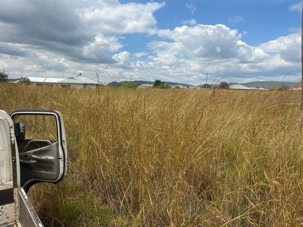 Property photo 2 of 4 Open Driver's Door Of A White Pickup Truck In A Tall Grassy Field With Houses And Hills Under A Cloudy Blue Sky.