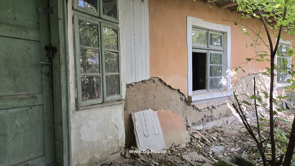 Property photo 2 of 32 Detailed View Of The House Wall Showing Peeling Plaster, A Green Wooden Door, And Windows Surrounded By Vegetation.