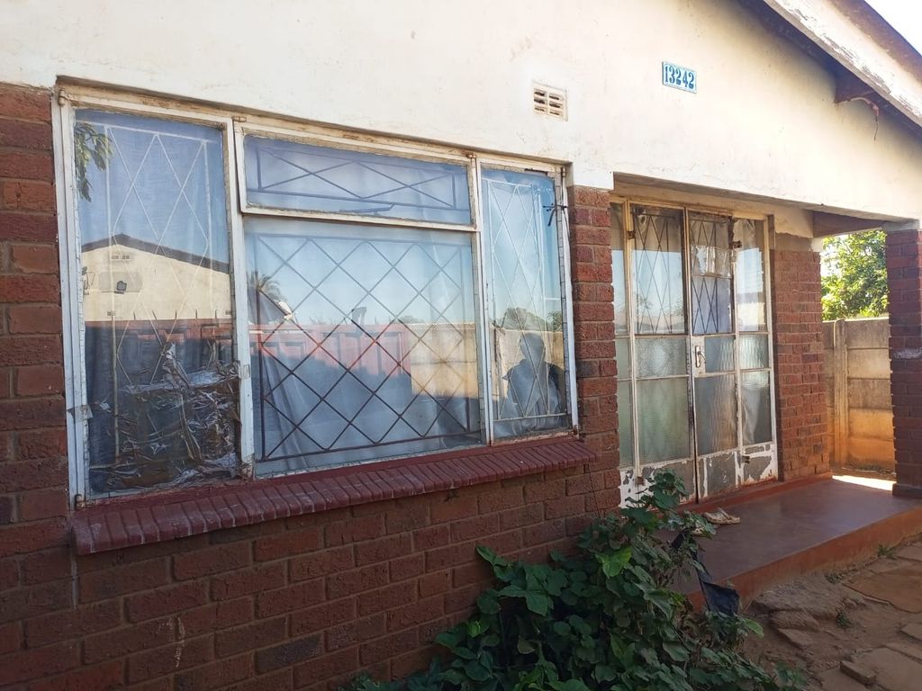 Property photo 2 of 12 Front View Of A Brick House With Large Glass Windows Secured By Metal Bars, Peeling White Paint, And Overgrown Plants Nearby.