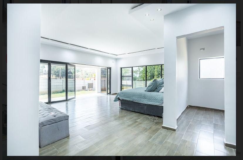 Property photo 3 of 19 Bright Modern Bedroom With Large Glass Doors Opening To A Garden, Featuring A Bed With Teal Bedding And A Gray Ottoman On A Light Wood Floor.