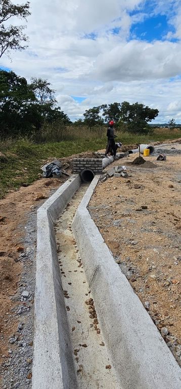 Property photo 1 of 2 Concrete Drainage Trench Under Construction With A Buried Pipe, A Worker In A Red Helmet Standing Nearby, And Scattered Materials On A Dirt Site.