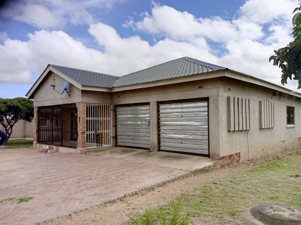 Property photo 1 of 9 Exterior Of A Single-Story House With Two Metal Roll-Up Garages And A Gated Entry On A Brick-Paved Driveway Under A Blue Sky