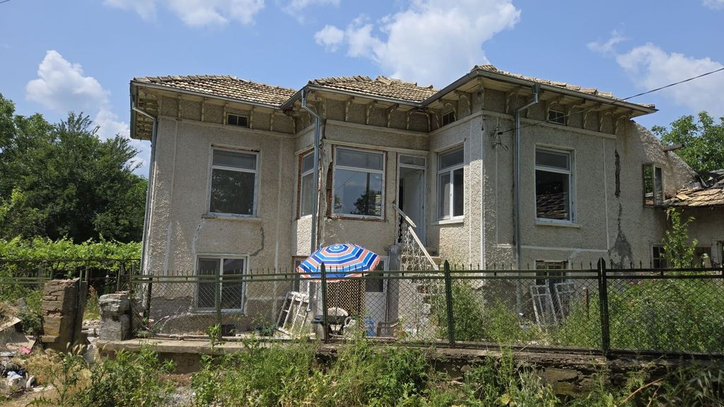 Property photo 1 of 40 Front View Of The Two-Storey Bulgarian House Showing Textured Walls, Multiple Windows, And A Small Outdoor Seating Area With A Striped Umbrella