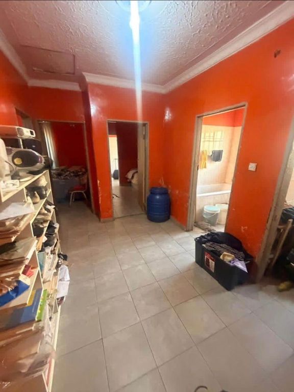 Property photo 2 of 9 Orange-Walled Hallway With Tiled Floor, A Cluttered Shelf To The Left, A Blue Water Drum, And Open Doors To Adjacent Rooms.