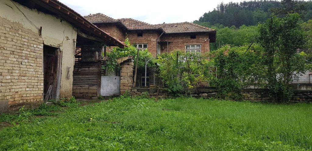 Property photo 1 of 100 View Of A Brick House With Tiled Roof And Green Garden Area Enclosed By Stone And Wire Fencing, With Forested Hills In The Background.