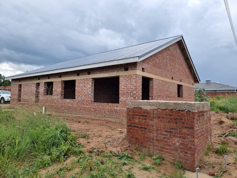 Property photo 1 of 12 Brick Building Under Construction With Open Window Openings And A Metal Roof, On A Dirt Lot With Overgrown Grass, Cloudy Sky Above