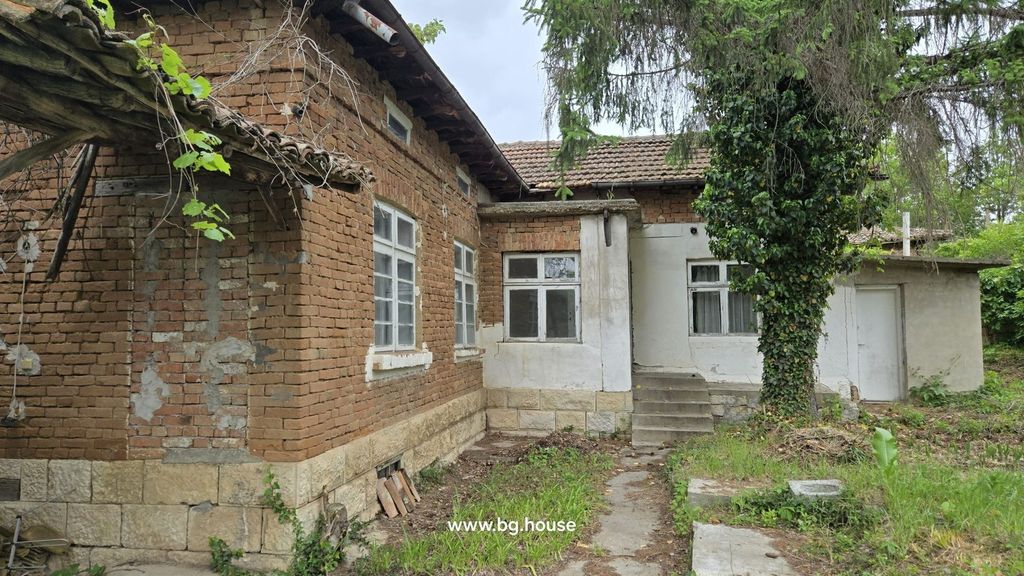 Property photo 1 of 26 Exterior View Of A Traditional Bulgarian Brick House With White Window Frames And A Tiled Roof, Set In A Garden With Trees And Plants.