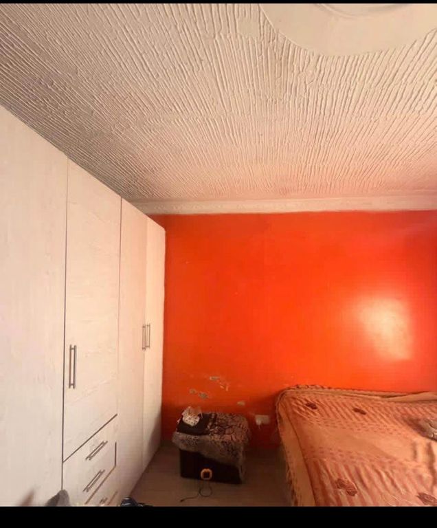 Property photo 3 of 9 Bedroom With An Orange Accent Wall, White Wardrobes Along The Left, And A Bed With A Beige Blanket On The Right; A Small Cushioned Stool And Scattered Items Sit At The Foot Of The Bed.
