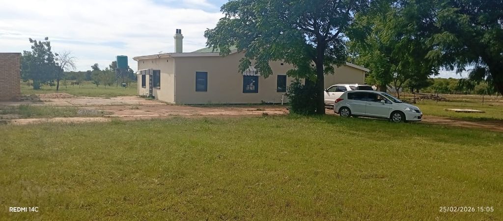 Property photo 3 of 12 Single-Story Beige Building With A Large Tree In Front, Two White Cars Parked To The Right On A Dirt Driveway, In A Grassy Rural Setting.