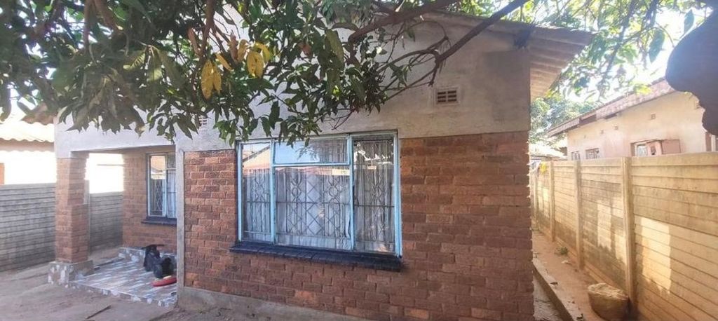 Property photo 1 of 7 Small Brick House With A Large Barred Front Window, A Dirt Yard, And A Tree Overhead.