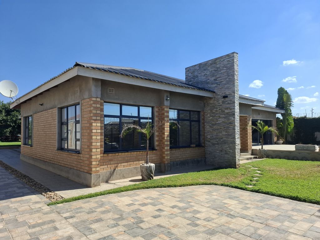 Property photo 1 of 20 Modern House Exterior With Brick Walls, Large Glass Windows, A Stone Chimney, And A Satellite Dish Against A Clear Blue Sky.