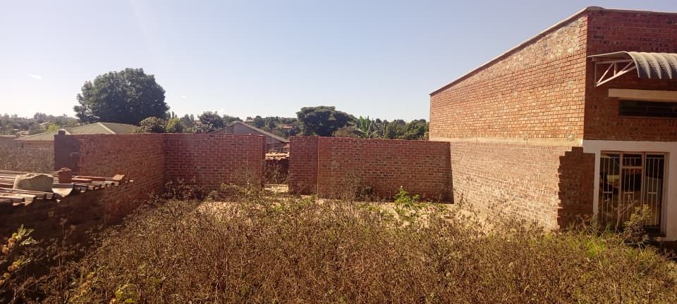 Property photo 1 of 5 Open Courtyard Surrounded By Red Brick Walls With Overgrown Vegetation In The Foreground And A Brick Building On The Right Under A Bright Sky.