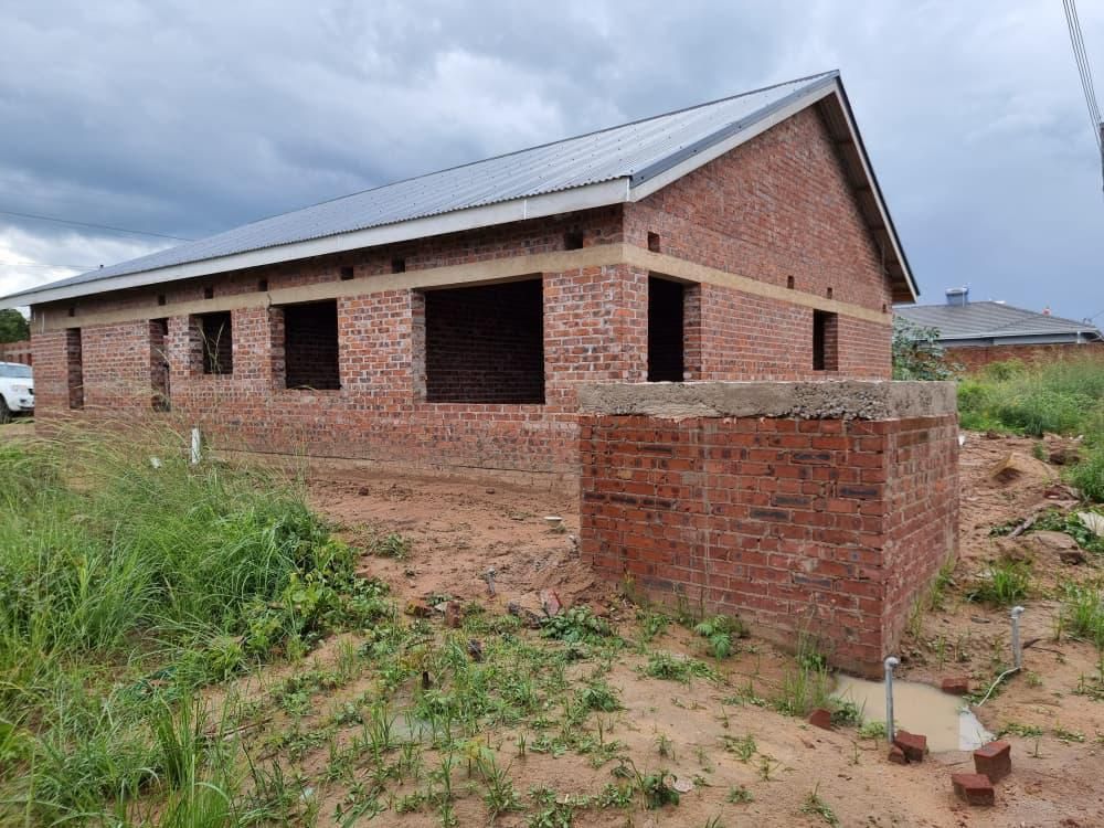 Property photo 2 of 12 Under-Construction Brick House With A Metal Roof On A Muddy Plot; Open Window Openings And Exposed Brick Walls Under A Cloudy Sky.