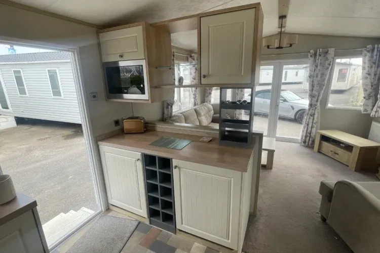 Property photo 3 of 10 A Caravan's Interior With White And Wood Accents, Showing Kitchen And Living Areas, With A Car Outside.