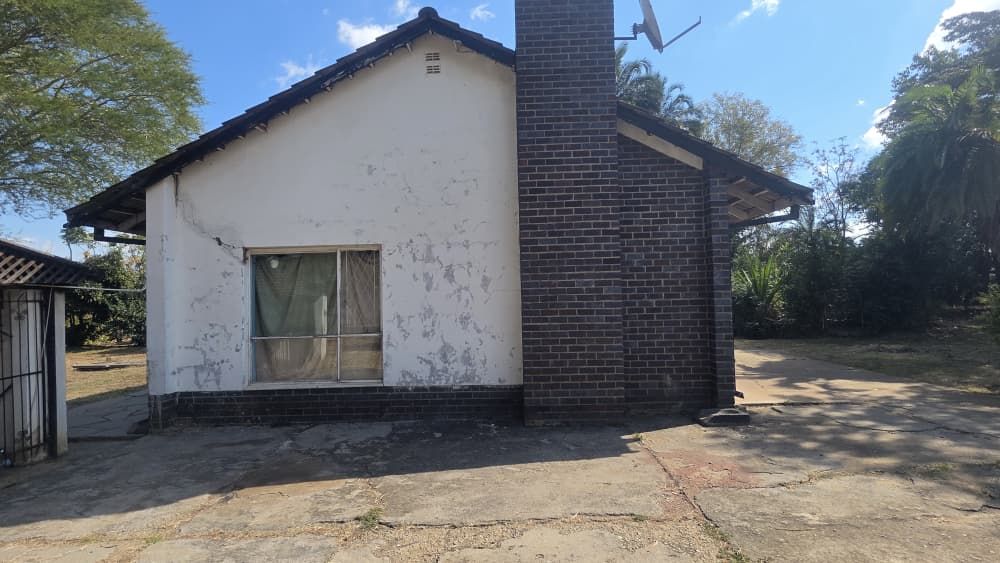 Property photo 3 of 12 Small Single-Story House With White Peeling Plaster, A Brick Chimney, And A Front Window With A Curtain Under A Sunny Sky.