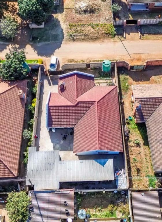 Property photo 2 of 6 Aerial View Of A Suburban Block: Red-Tiled Roofs, A Dirt Road, A White Car Parked Along The Street, And A Green Water Tank In A Yard.