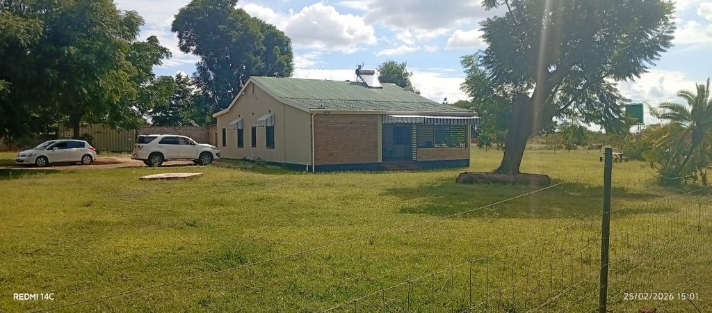 Property photo 2 of 12 Small Beige, Single-Story Building With A Green Metal Roof, Two White Cars Parked Beside It, A Grassy Yard And Trees, And A Wire Fence In The Foreground.